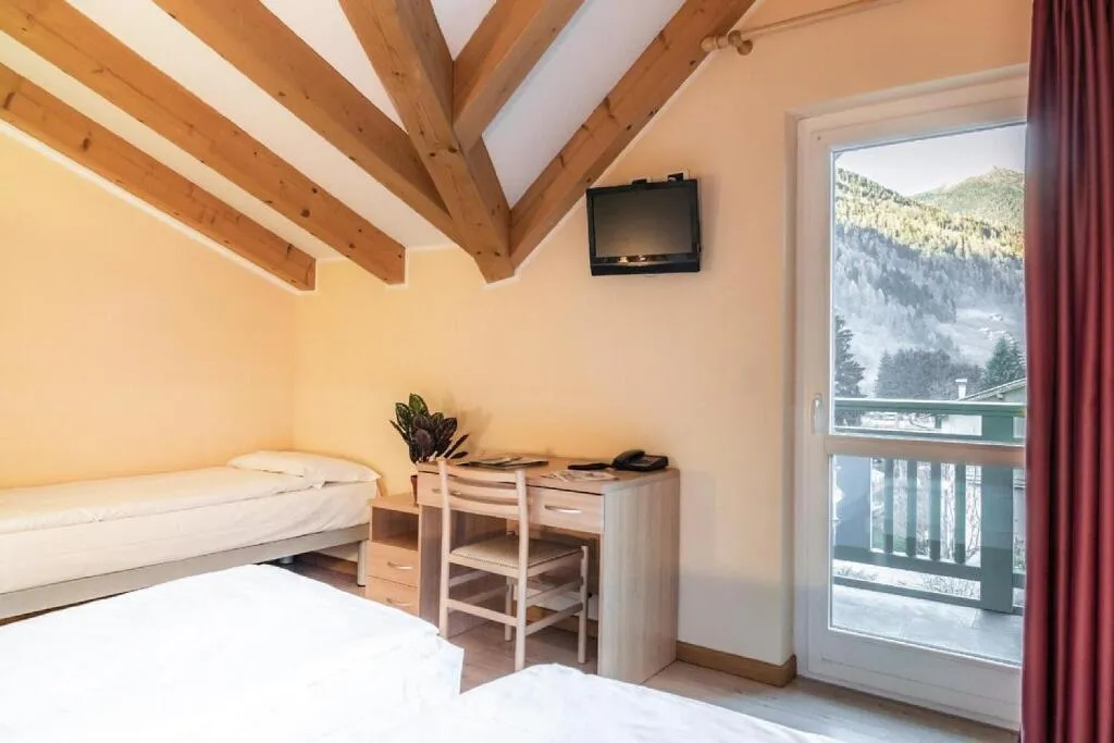 Camera con letto singolo, scrivania, TV e balcone con vista sulle montagne