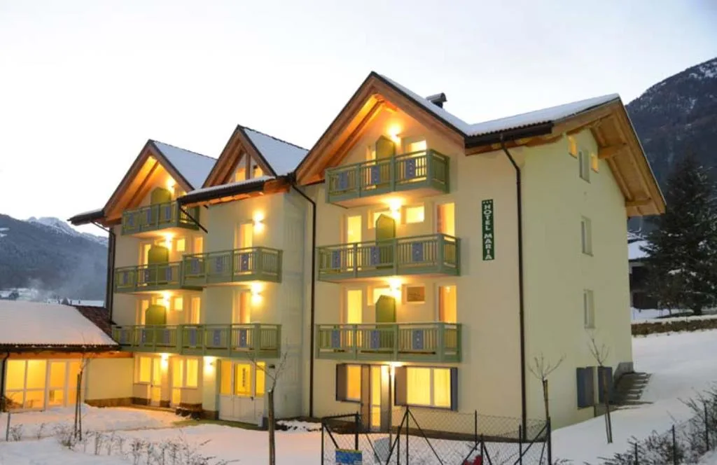 Facciata dell'Hotel Maria al crepuscolo con balconi e paesaggio innevato