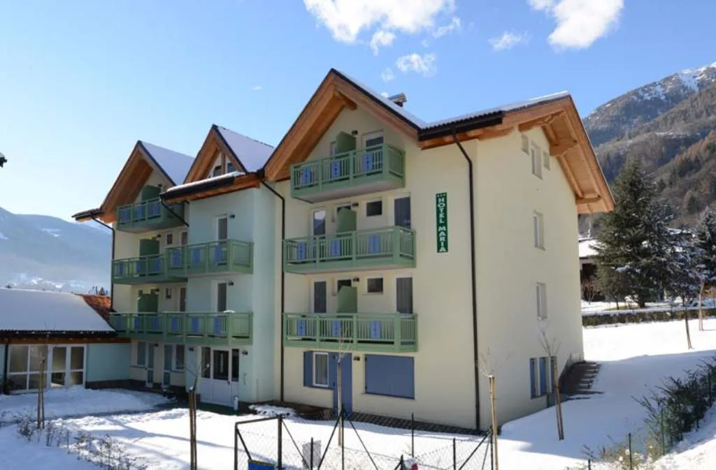 Esterno dell'Hotel Maria con balconi verdi e montagne in giornata di sole