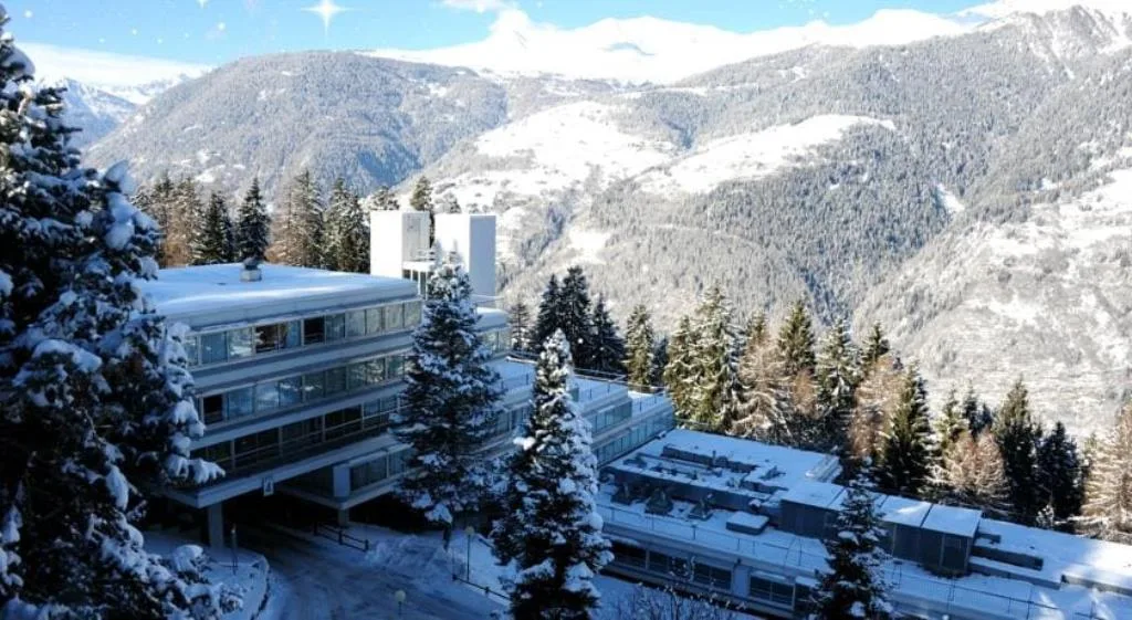 Edificio dell'hotel innevato circondato da abeti e vallata montana