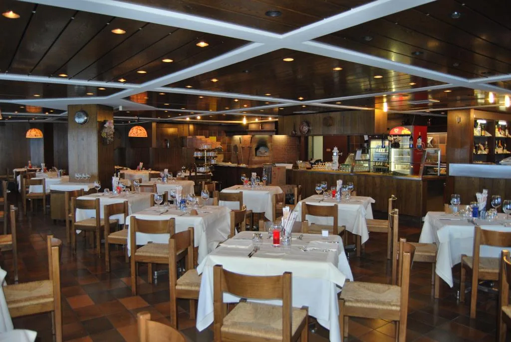 Sala ristorante con tavoli apparecchiati, sedie in legno e forno a vista