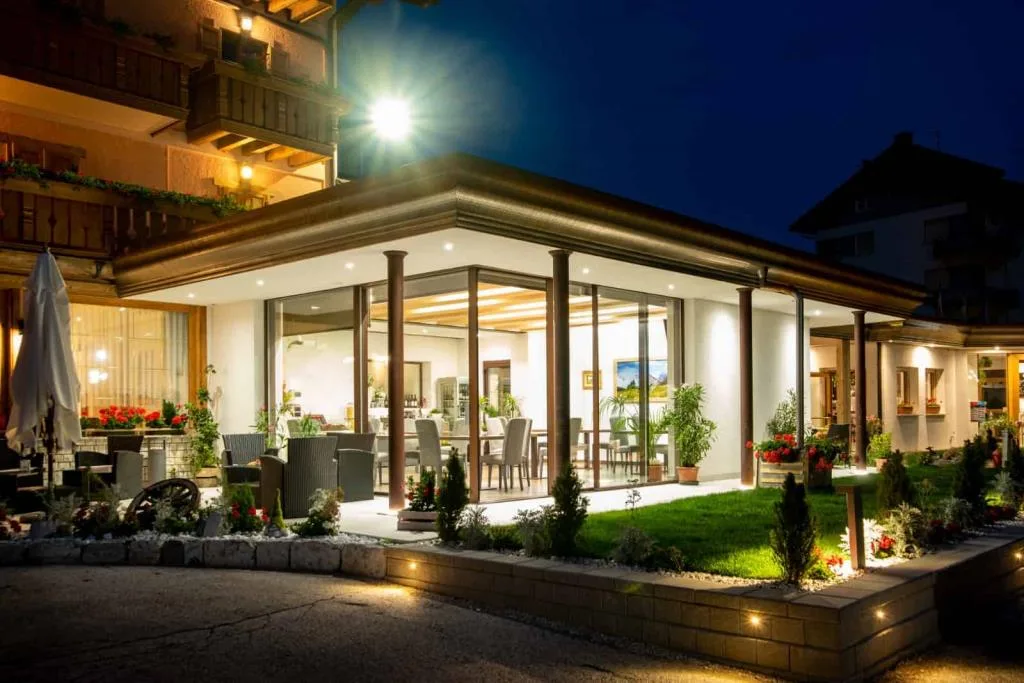 Veranda a vetri del ristorante illuminata di sera con giardino curato