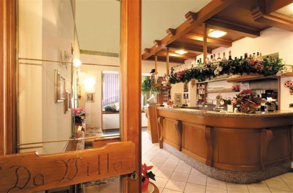 Zona bar dell'hotel con bancone in legno e porta a vetri decorata con scritta Da Villa