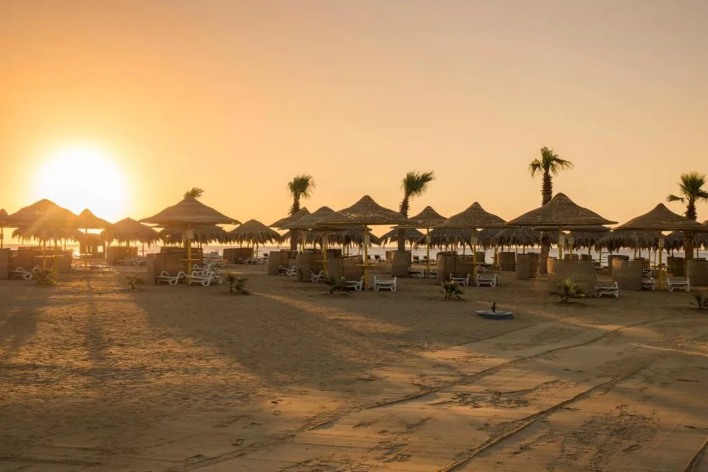 Spiaggia con ombrelloni di paglia e palme illuminata dalla calda luce del sole al tramonto