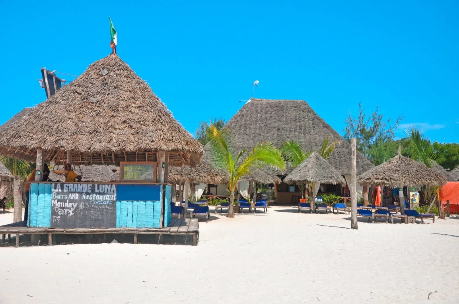 Bar e ristorante sulla spiaggia con capanne dal tetto in paglia e sabbia bianca sotto cielo azzurro
