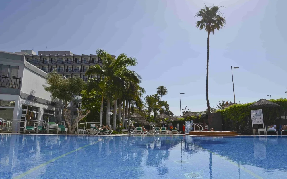 Piscina con acqua limpida, palme alte e edificio dell'hotel sullo sfondo